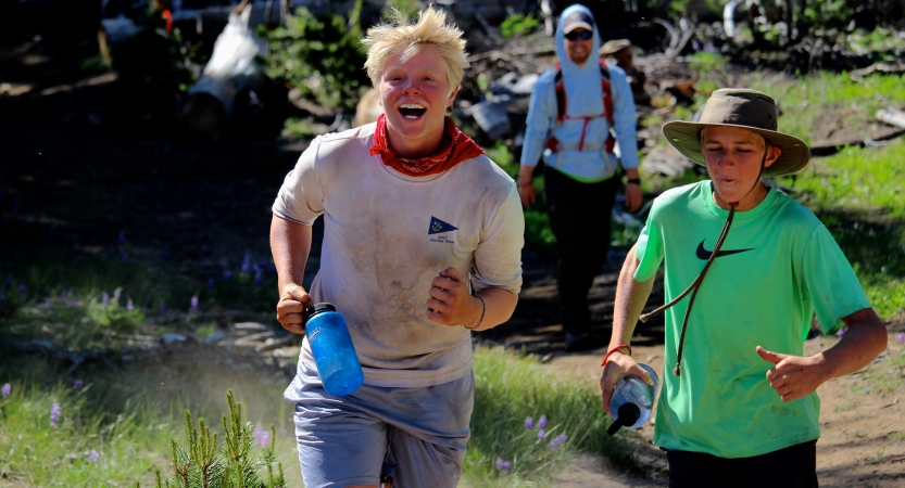 two students jog through grass and smile at the camera